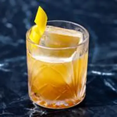 Gold Rush cocktail in an engraved rocks glass with single large ice cup and lemon twist, on a dark marble background