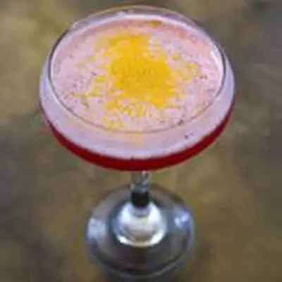 A top down shot of a cocktail coupe filled with a red drink topped with gold flakes. 