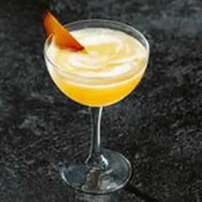 orange-hued Slivopolitan cocktail in a coupe glass, garnished with a fresh plum slice