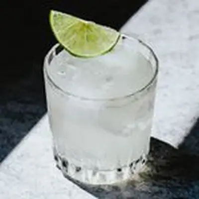 Golden Glove cocktail in a rocks glass with a half lime wheel, served in a sunbeam on a white textured surface