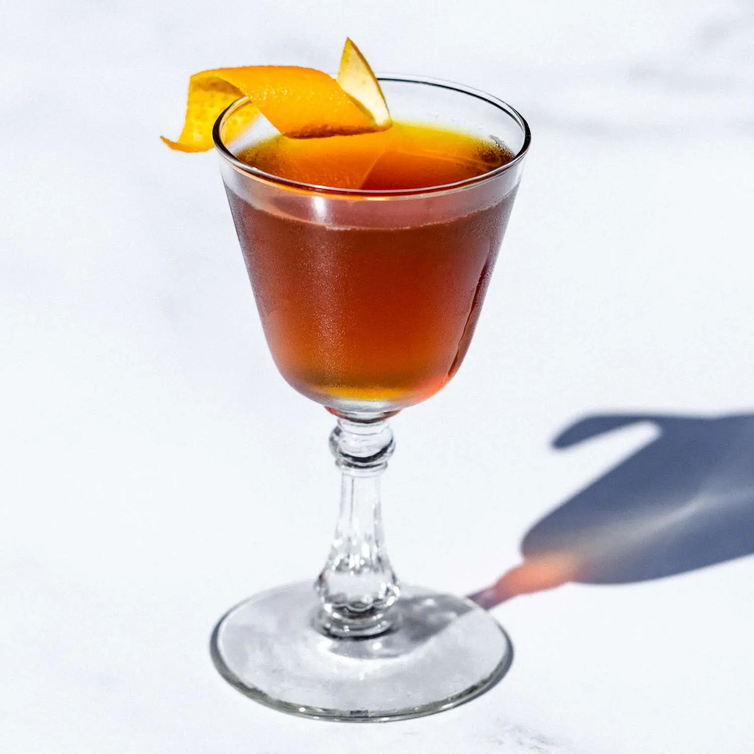 Manhattan Transfer cocktail in vintage style Nick & Nora glass, with orange twist garnish on rim