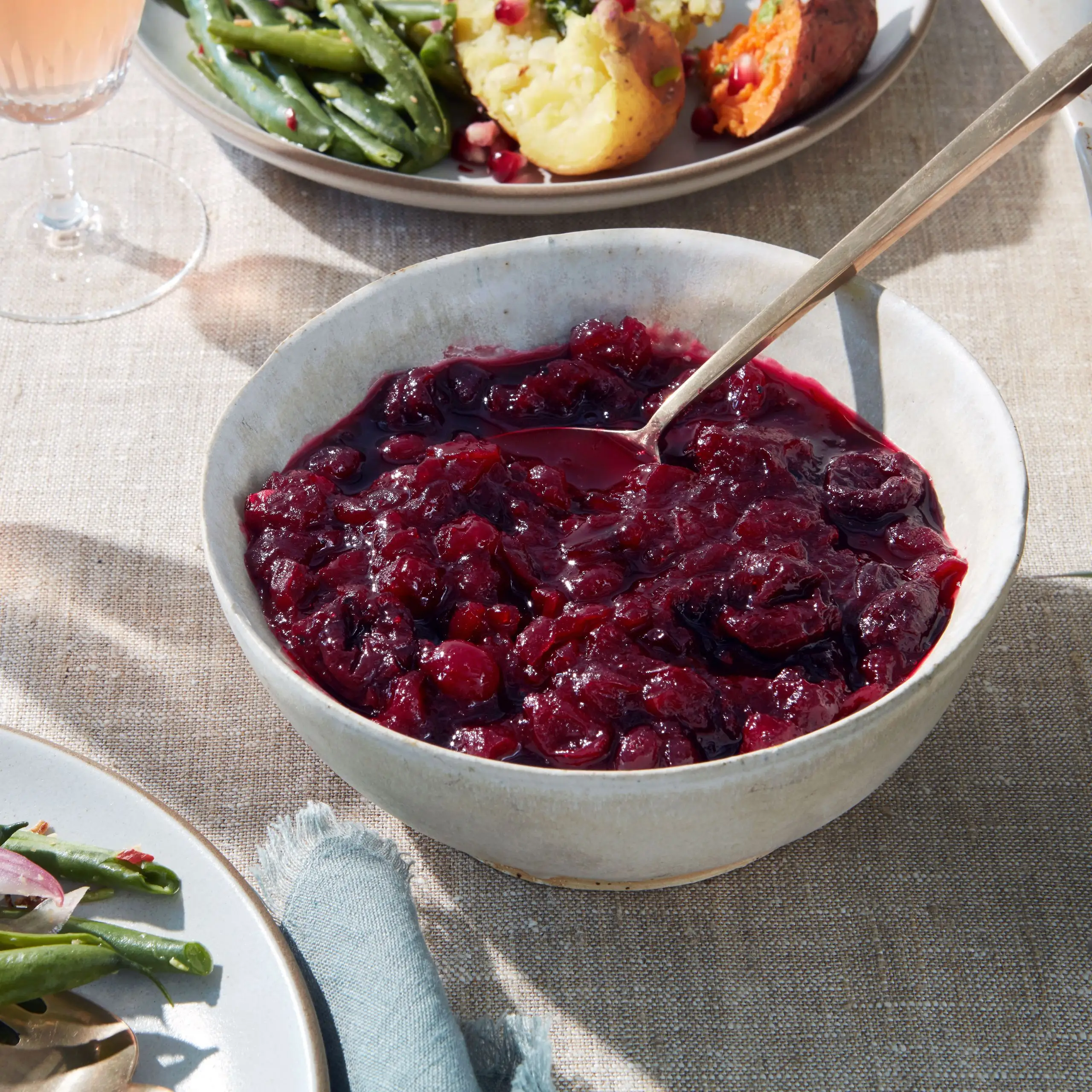 Threequarter shot of a deepred cranberry sauce on an elegant Thanksgiving table laid with a linen tablecloth.