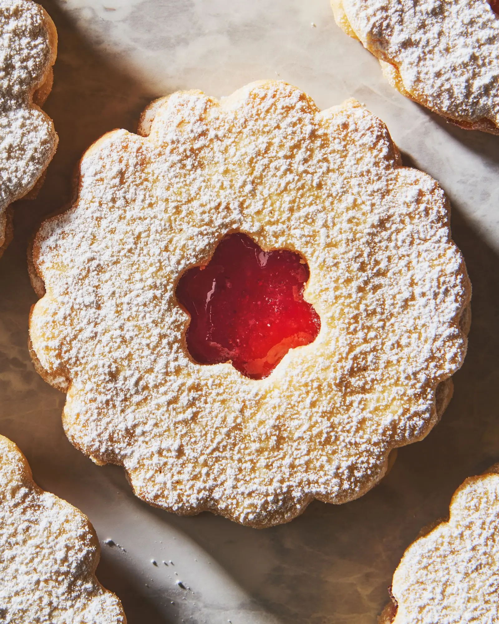 A roundshaped linzer cookie with raspberry jam topped with powdered sugar.