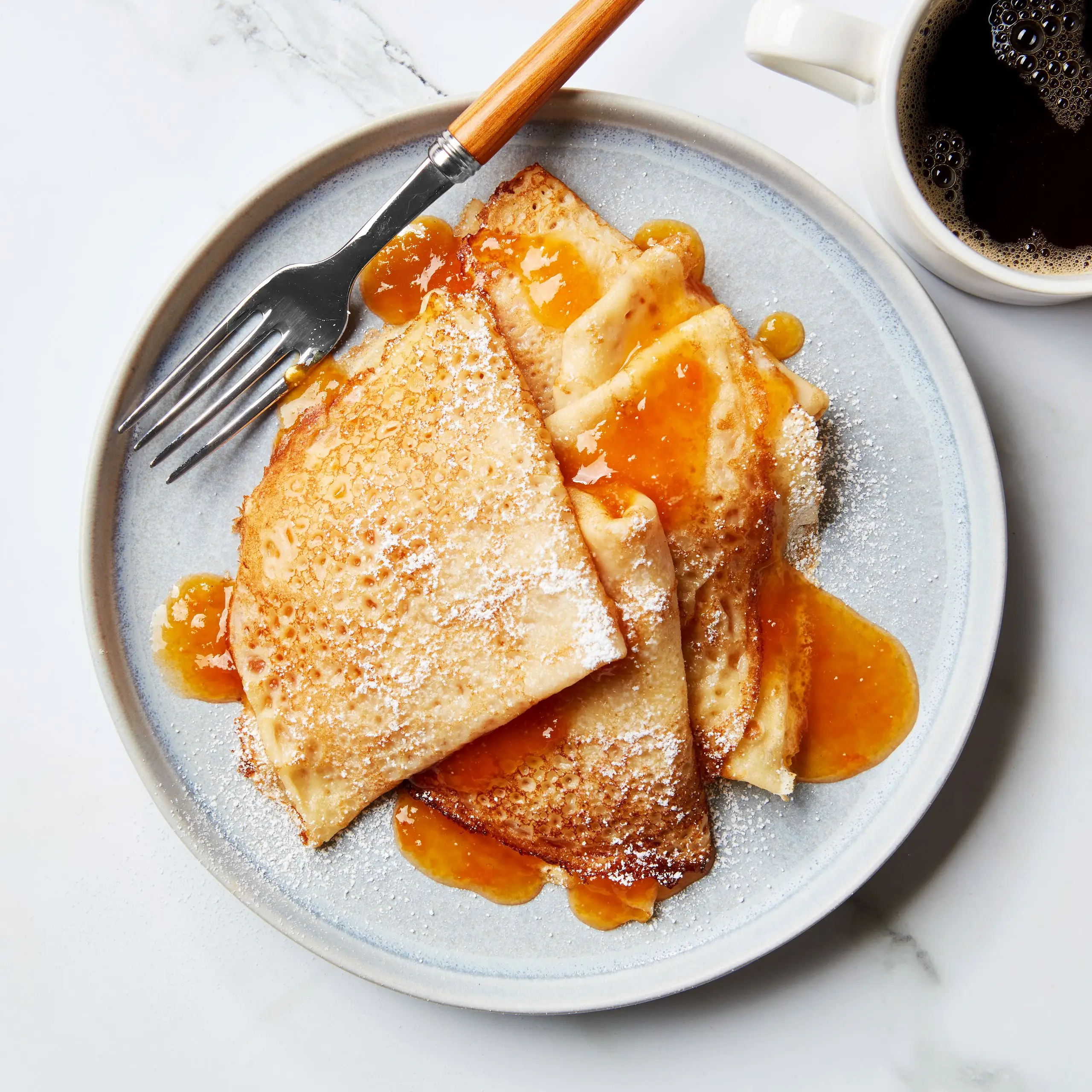 Folded crepes with apricot jam and powdered sugar on a plate.