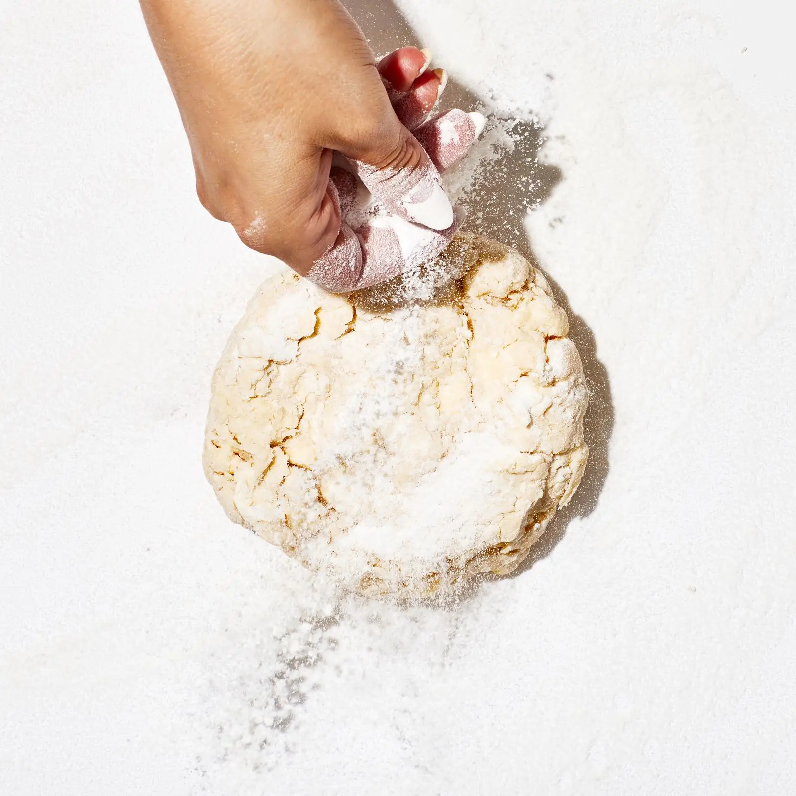 Hand sprinkling flour over dough.