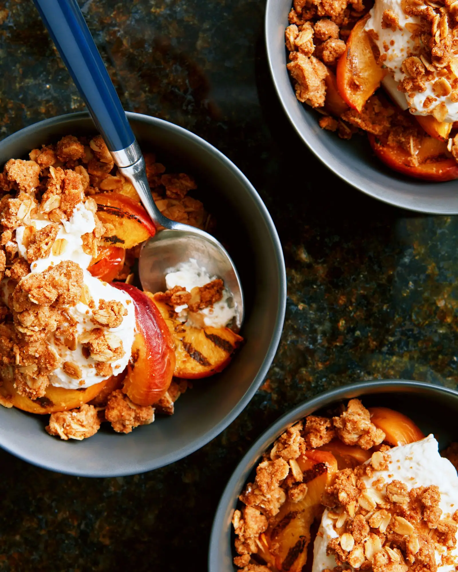 Bowls of oat crumble topping with whipped cream and grilled peaches.