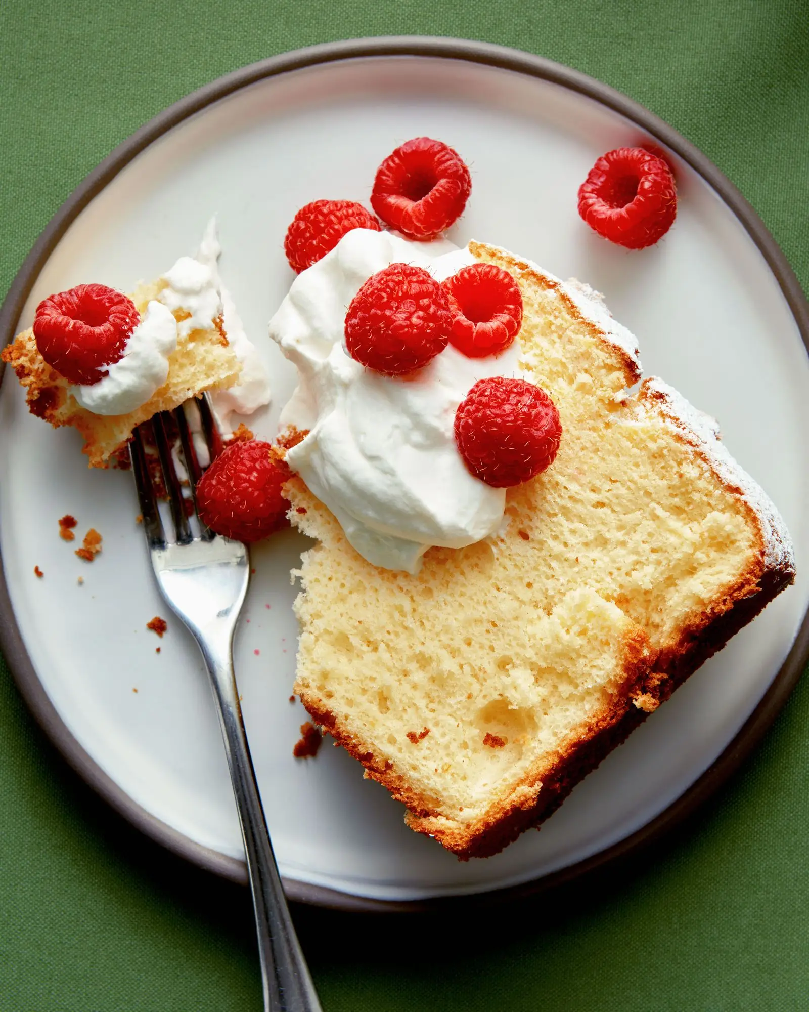 A slice of lemon chiffon cake baked in a tube pan dusted with confectioners sugar and served with raspberries and...
