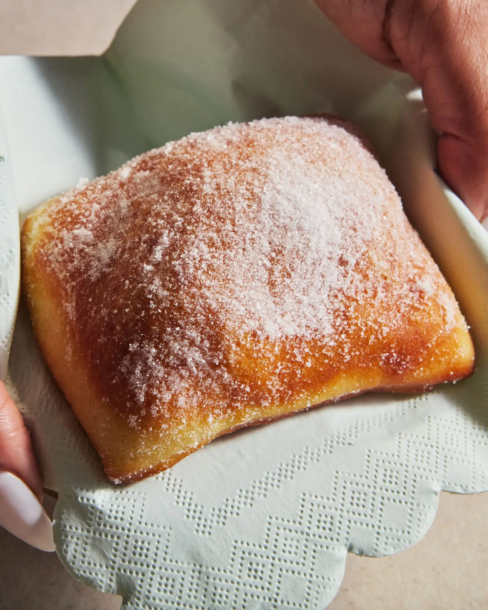 Hands holding a malasada in a napkin.