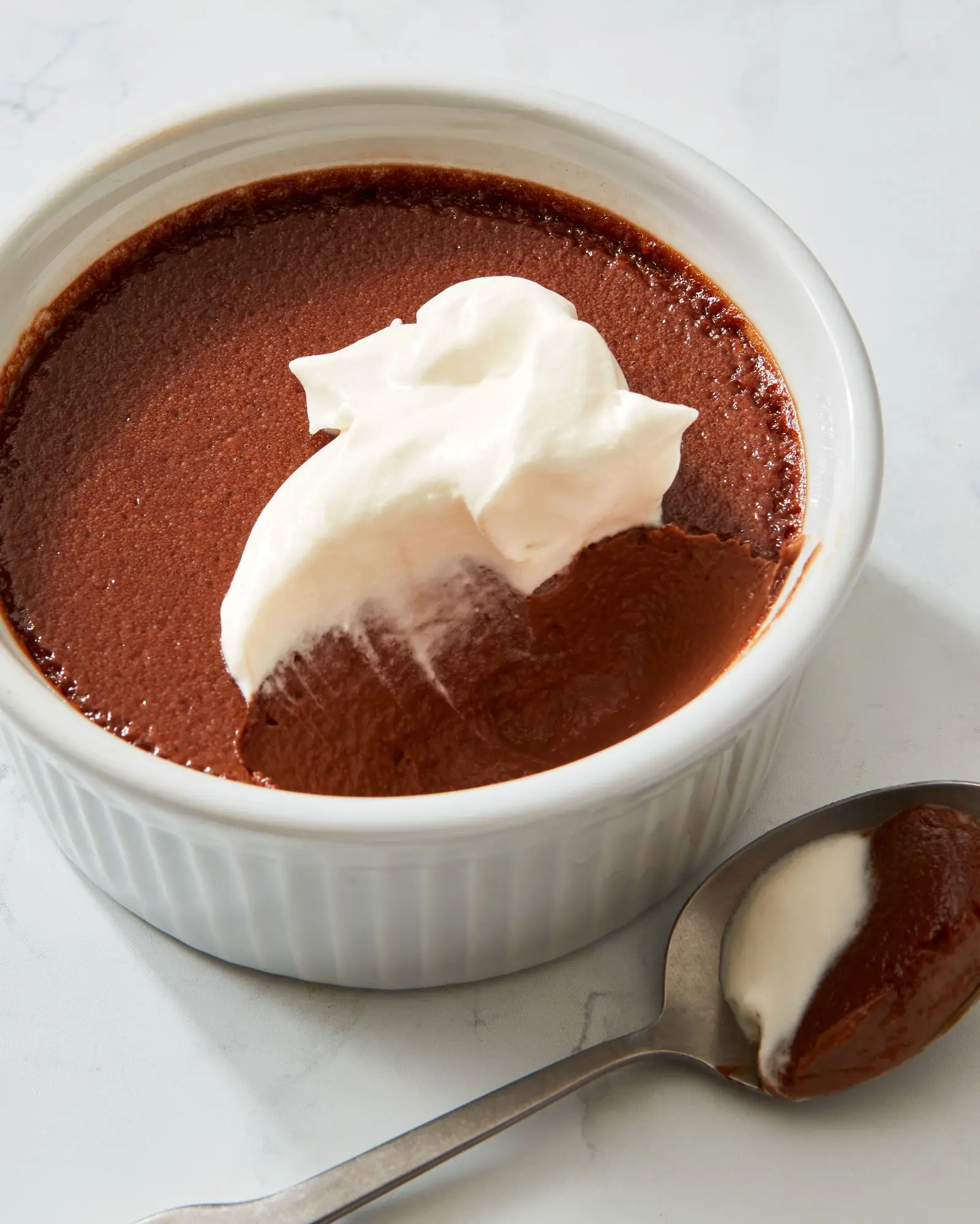 Chocolate pots de crème and whipped cream in a ramekin.