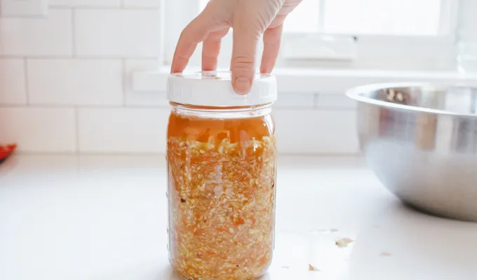 Screwing a plastic lid on top of the jar of homemade sauerkraut.' title='Easy Spicy Sauerkraut Recipe
