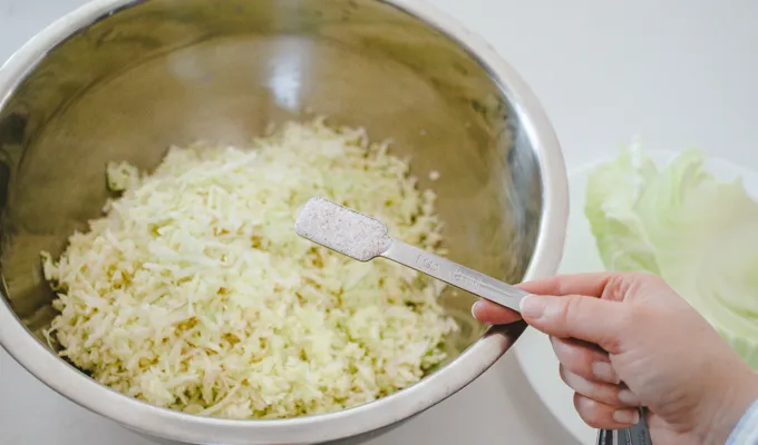 Sprinkling salt on shredded cabbage for homemade spicy sauerkraut.' title='Easy Spicy Sauerkraut Recipe