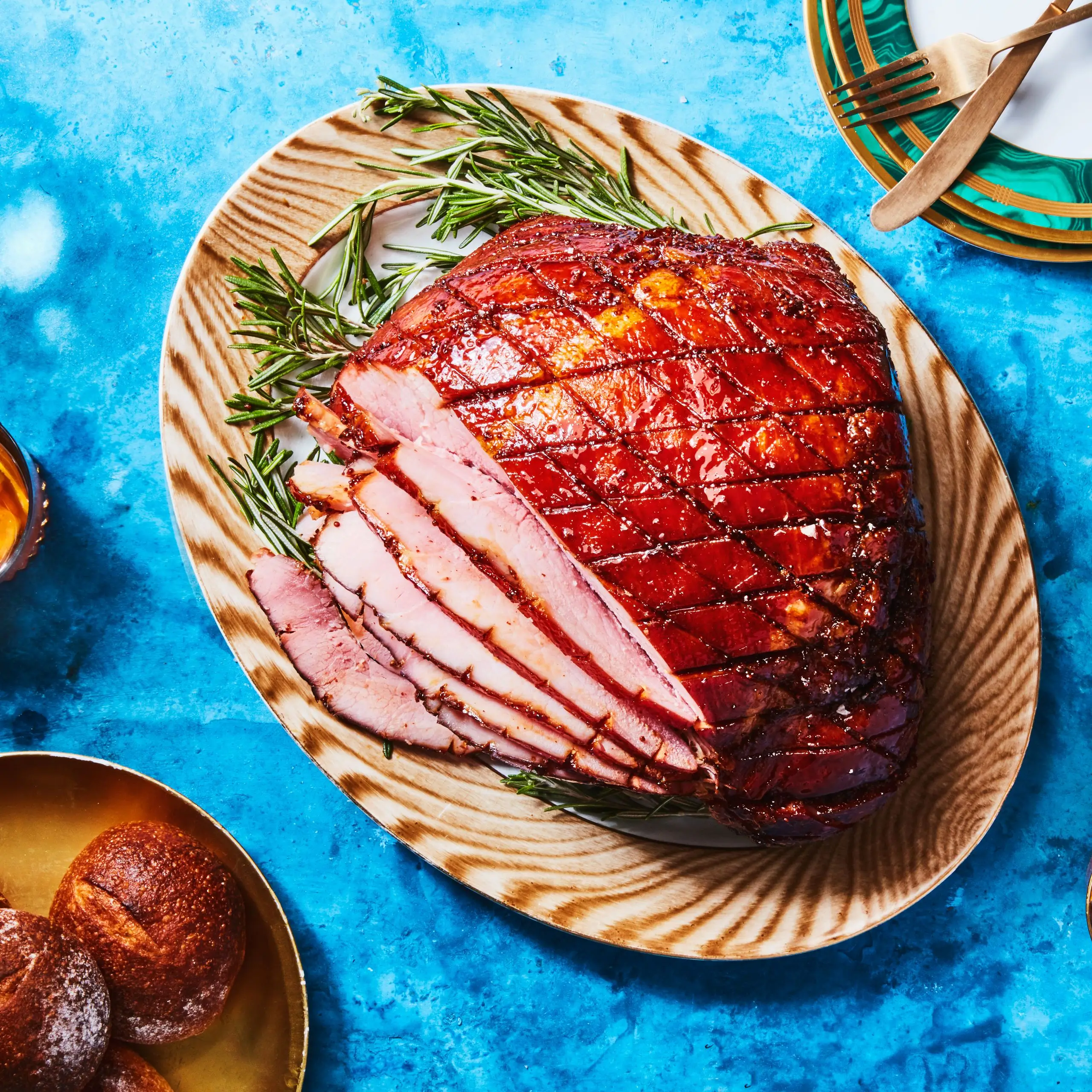 A partially sliced Christmas ham coated in a brownsugarandmustard glaze set on a platter garnished with rosemary atop a...
