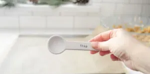 A hand holding a white teaspoon measuring spoon.' title='No Bake Peanut Butter Balls without Chocolate