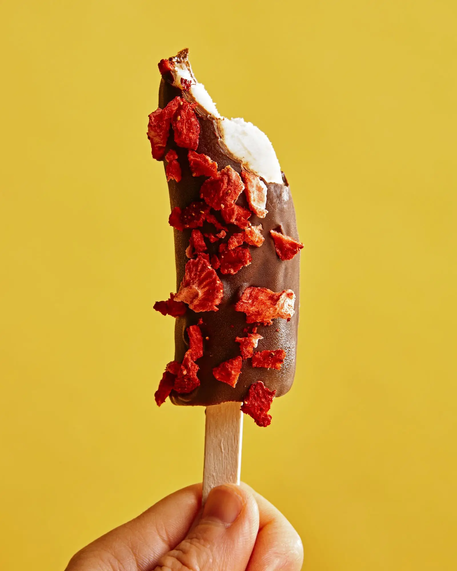 A single chocolate covered banana topped with freeze dried strawberries.
