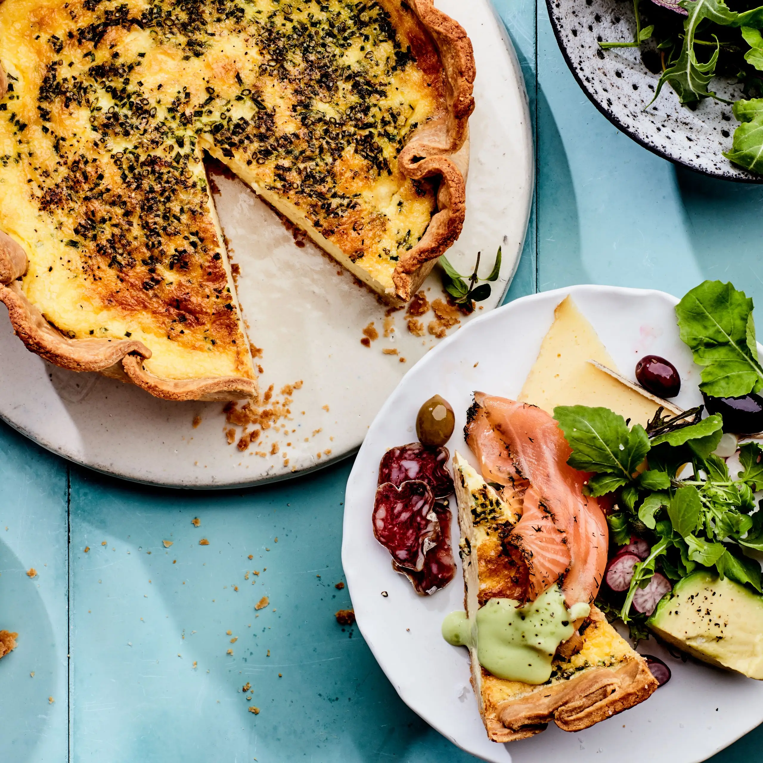 Deep dish quiche on a plate. Next to it is another plate with a slice of quiche and green salad.