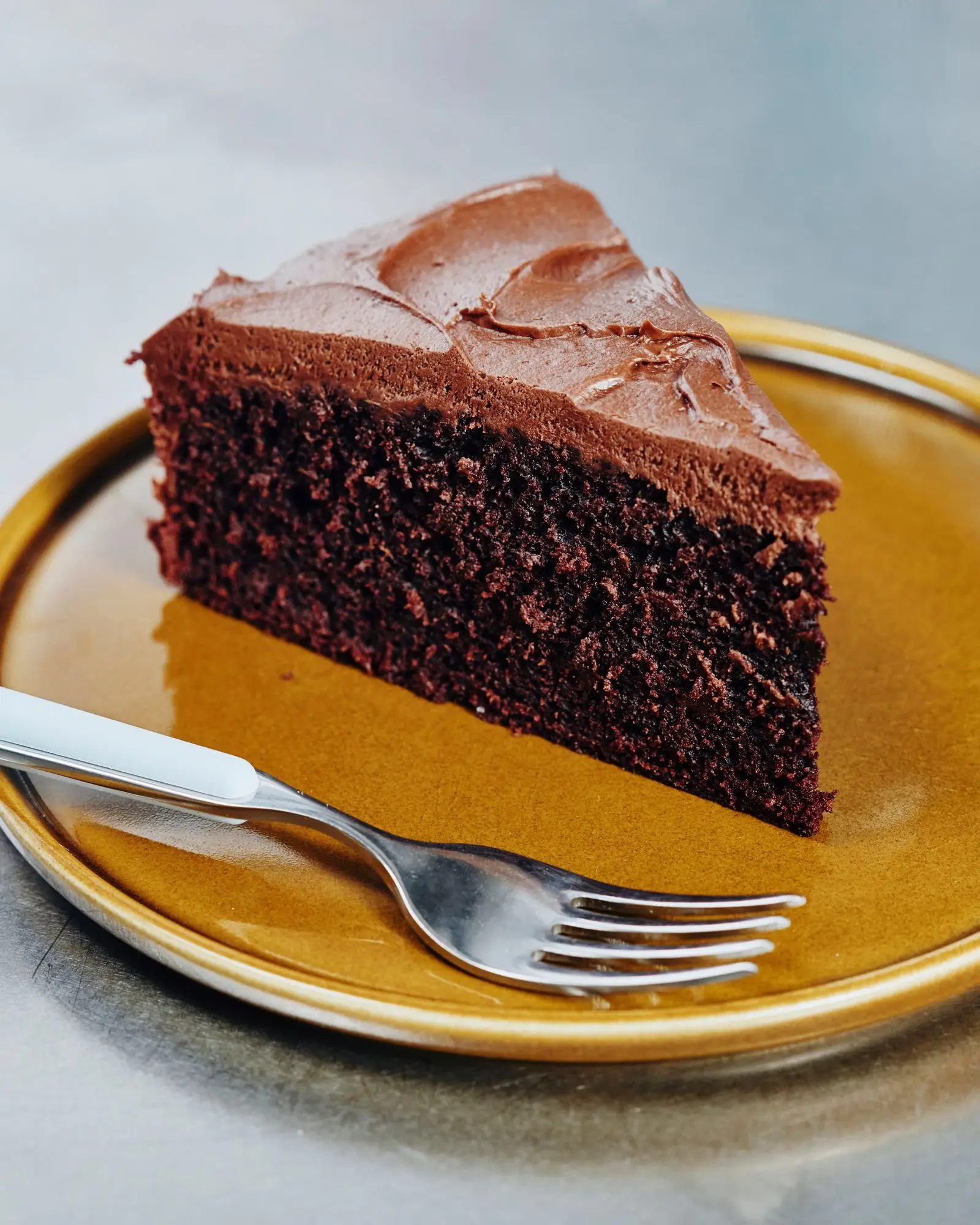 A slice of Chocolate Cream Cheese Frosted cake on a kitchen table.Placed on a yellow plate