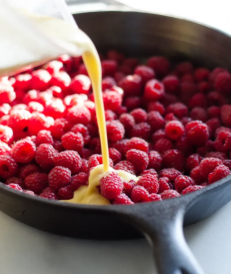 Pouring the batter over the berries in the bottom of the cast iron skillet. ' title='Raspberry Clafoutis