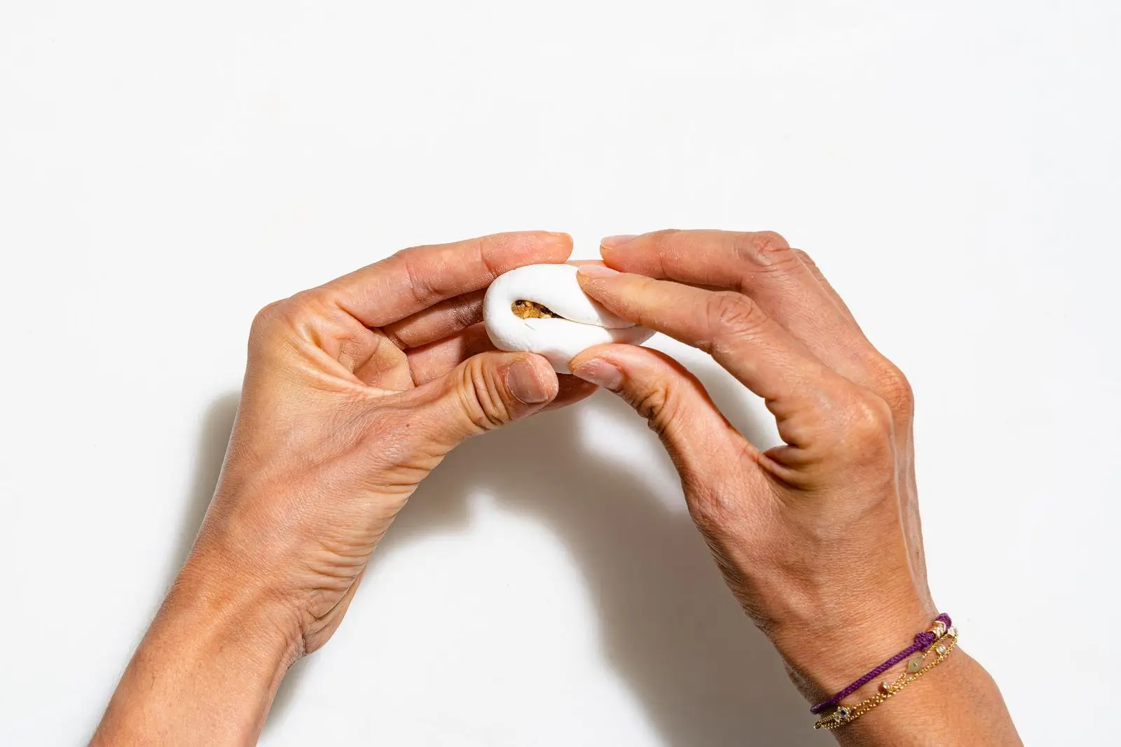 Hands rolling a rice blossom over a white surface.