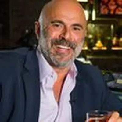 Tony Abou-Ganim headshot, seated at bar smiling while holding a Negroni