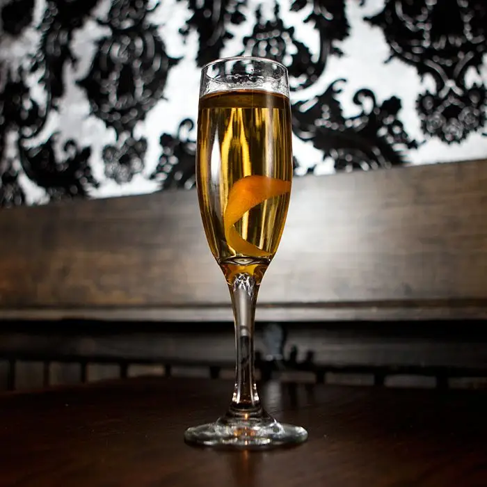 La Tour Eiffel cocktail in champagne flute with orange peel against background with black and white wallpaper and wood