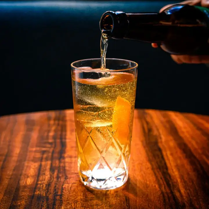 Hard cider being poured into Saison Highball glass on wooden tabletop