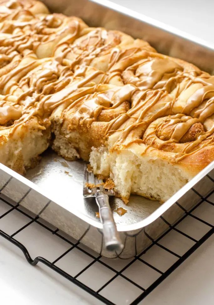 A pan of cinnamon rolls without milk with a couple of rolls taken out and a fork in the pan.' title='Cinnamon Roll Recipe Without Milk