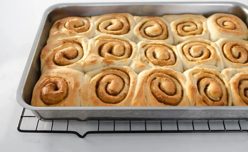The baked cinnamon rolls without milk in a pan on a wire cooling rack.' title='Cinnamon Roll Recipe Without Milk