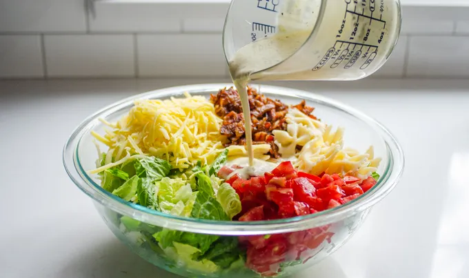 Pouring the dressing on top of the ingredients.' title='BLT Bowtie Pasta Salad