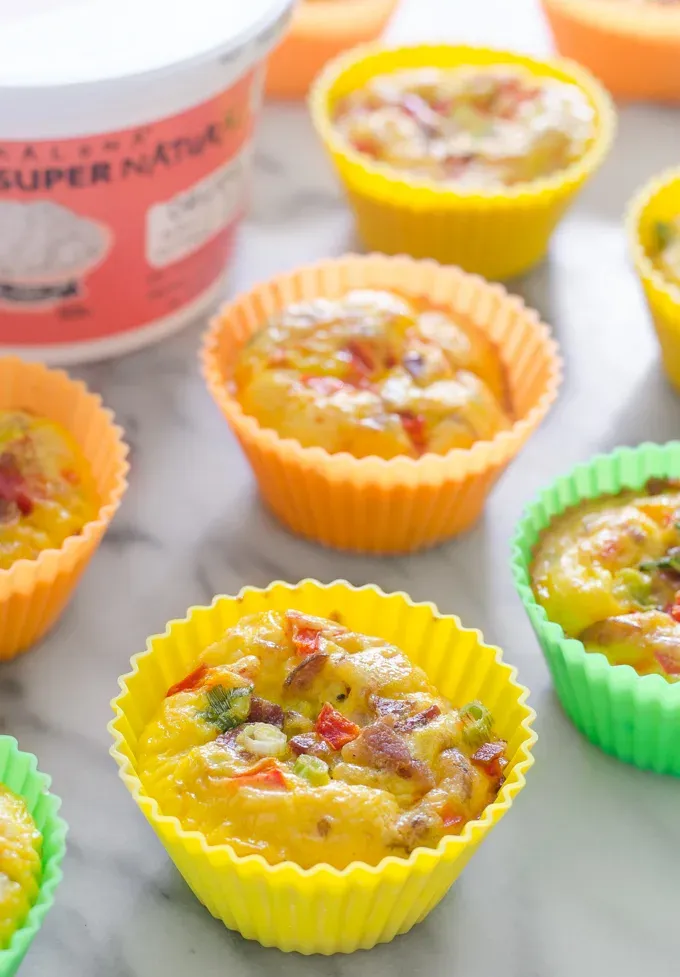 Several egg muffins on a marble surface with Kalona SuperNatural cottage cheese in the background.' title='Egg Muffin Cups with Cottage Cheese Bacon and Peppers