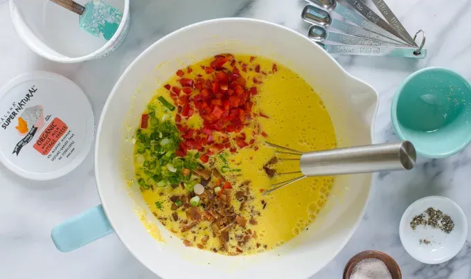 Bacon green onions and red bell peppers in the mixing bowl with the egg mixture.' title='Egg Muffin Cups with Cottage Cheese Bacon and Peppers