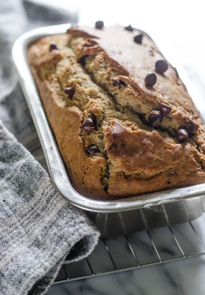 Sourdough banana bread in loaf pan on a cooling rack on a marble surface.' title='Sourdough Banana Bread