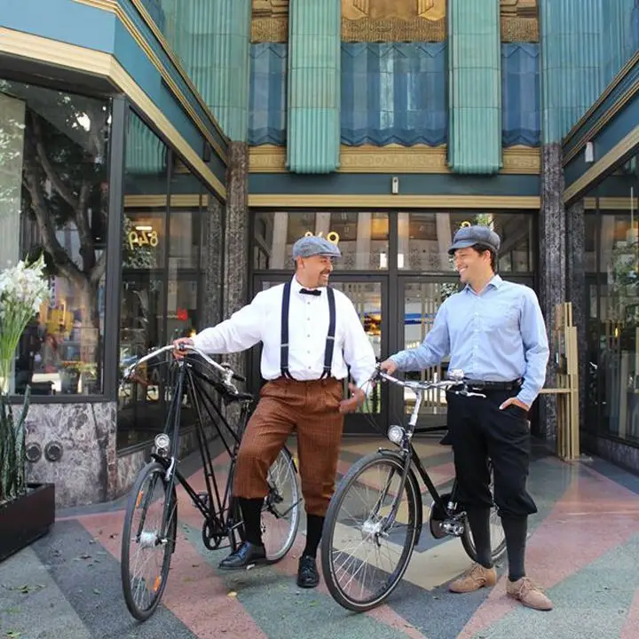 Two men standing with bikes, wearing porkpie hats.