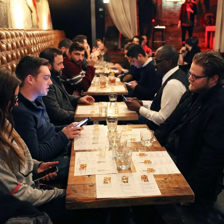 Tour participants sitting at several tables in a bar with whiskey glasses before them.