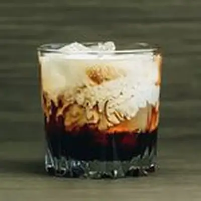 White Russian in a rocks glass, showing cream swirling with dark coffee liqueur