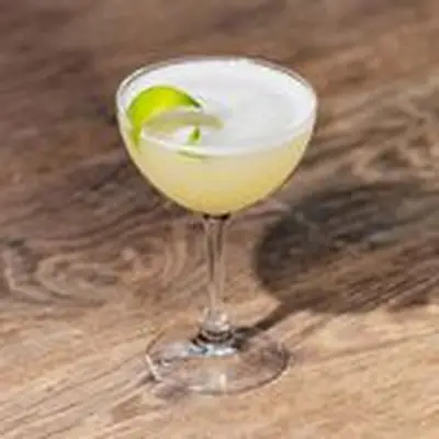 Daiquiri in coupe glass with light foam and lime twist on top, on wood counter