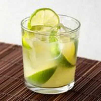Caipirinha cocktail in a rocks glass with limes, served on a bamboo mat
