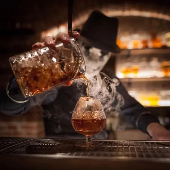 A smoking cocktail being poured from a mixing glass into a snifter at AnonymouS Shrink’s Office