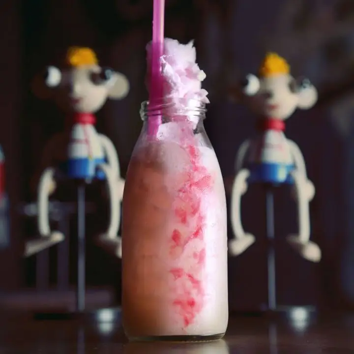A cocktail at Super Panda Circus. It is served in a small milk bottle of sorts and tufts of pink cotton candy are pulling over the top of the glass near a pink straw