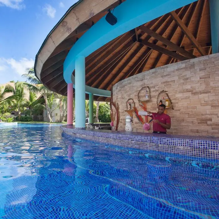 Majestic Colonial Punta Cana swim-up bar. A bartender pours a drink from behind a tiled bar jutting from the pool