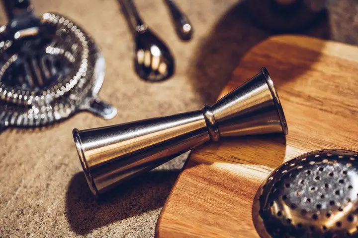A Japanese-style jigger on its side surrounded by various metal bar tools