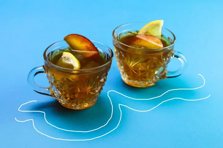 Two tea cocktails in clear tea cups garnished with lemon and peach slices