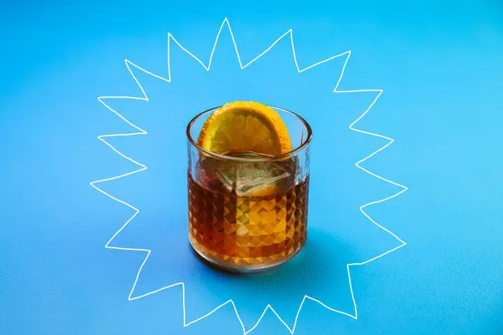 An Old Fashioned-style drink in a beveled rocks glass garnished with an orange wheel