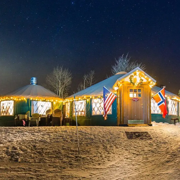 The Viking Yurt. Snow blankets the ground in front and bright lights glow from the charming yurts
