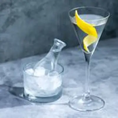 Dry Martini in a v-shaped martini glass with lemon twist, and a sidecar on extra Martini in chilled carafe in the background