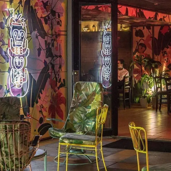 Junglebird bar in san juan. high-backed lounge charis are covered in palm-leaf upholstery and a neon tiki sign is on one wall