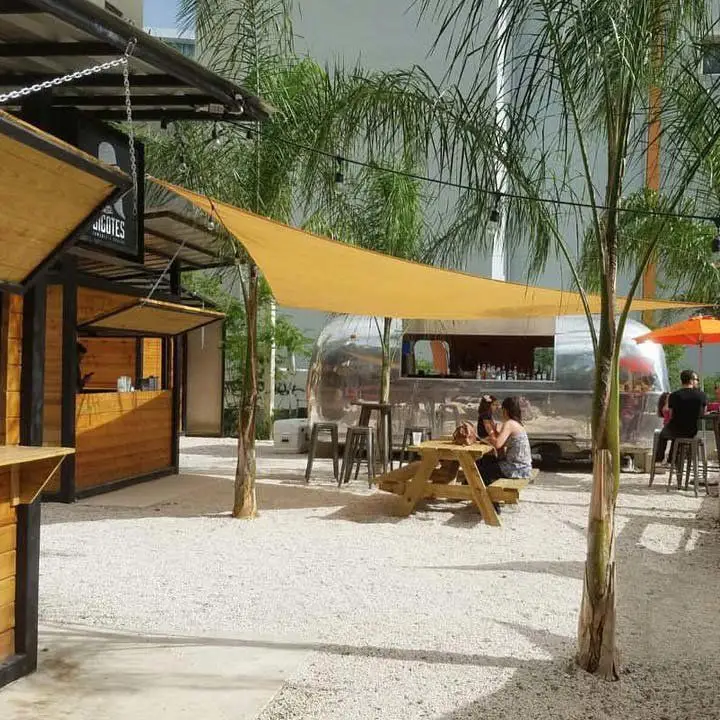 Caneca Coctelería Movil Airstream trailer in San Juan. an outdoor seating area with blond-wood picnic tables and slung canopies