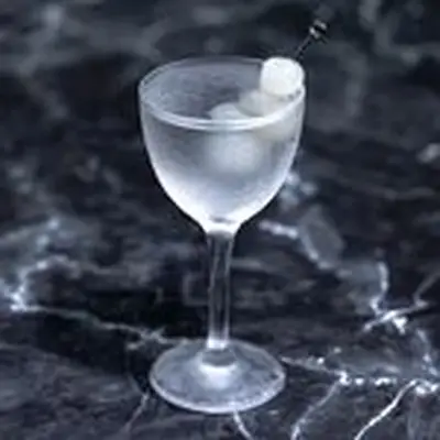 Gibson martini in an etched Nick & Nora glass on marble background, showing signature cocktail onion garnish on a metal pick
