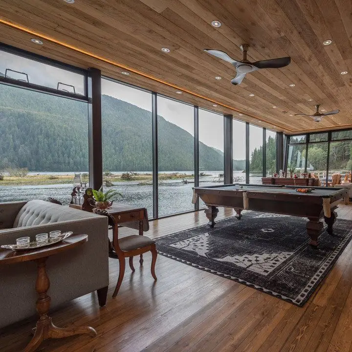 Clayoquot Wilderness Resort’s Ivanhoe Glass Lounge Bar interior with floor-ceiling glass windows and views right onto a river
