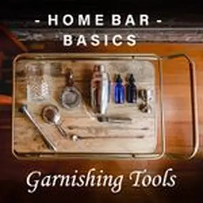 A cocktail mixing glass, two strainers, a shaker, peeler, two stoppered glass bottles, a metal jigger, two long-handled bar spoons, and a muddle rest on an elegant wooden bar tray with brass handles. A text overlay reads Home Bar Basics, Garnishing Tools.