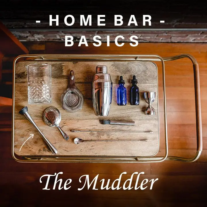 Aerial view of a wooden bar cart with various supplies and tools laid out, including a mixing glass, strainers, bar spoon, jigger and muddler